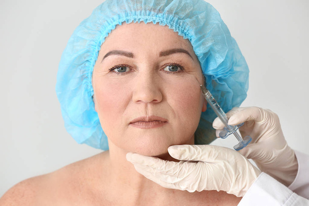 Mature woman receiving injection in face on light background - Fotó, kép