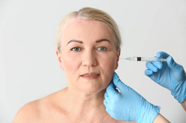 Mature woman receiving injection in face on light background - Foto, afbeelding