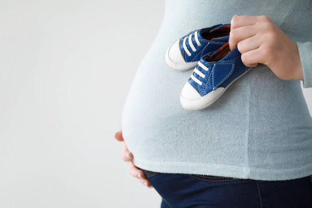 Hermosa mujer embarazada con botines de bebé sobre fondo claro
 - Foto, imagen
