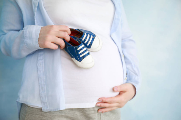 schöne schwangere Frau mit Babybooties auf farbigem Hintergrund, Nahaufnahme - Foto, Bild