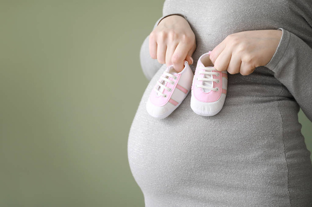 Krásná těhotná žena s dětskou botou na barevném pozadí, v šatně - Fotografie, Obrázek