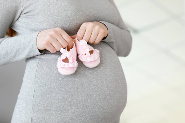 Mulher grávida bonita com botas de bebê em casa, close-up
 - Foto, Imagem