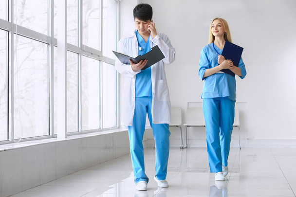 Mieslääkäri ja naispuolinen lääkintäavustaja kävelemässä käytävää pitkin klinikalla
 - Valokuva, kuva