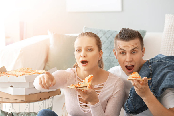 Emotioneel koppel eten smakelijke pizza terwijl TV kijken thuis - Foto, afbeelding