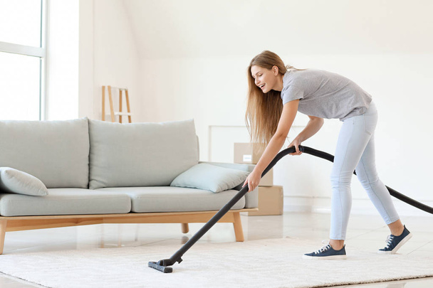 Young woman hoovering carpet at home - Foto, imagen