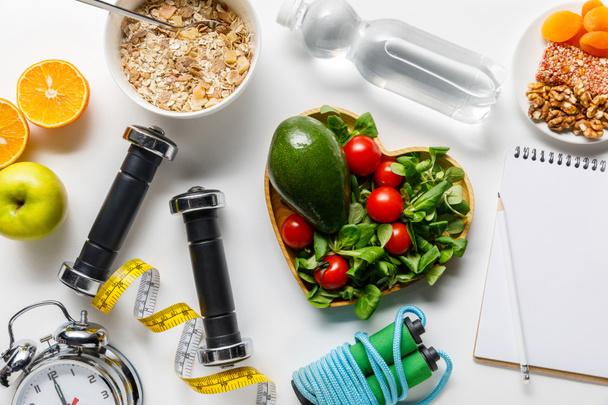 top view of sport equipment, measuring tape, alarm clock and notebook near diet food and water on white background - Photo, Image
