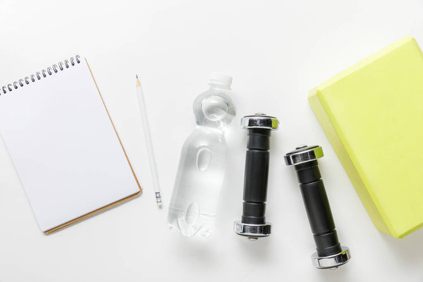top view of water in bottle, dumbbells and blank notebook with pencil near box on white background - Foto, immagini