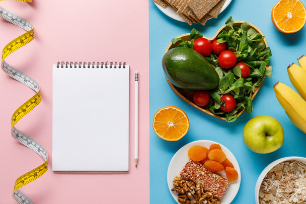 top view of diet food on blue and empty notebook with pencil and measuring tape on pink background - Photo, Image