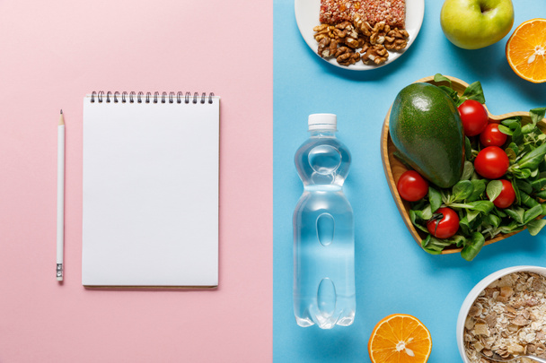 vista superior de la botella con agua y alimentos dietéticos cerca del cuaderno en blanco sobre fondo azul y rosa
 - Foto, Imagen