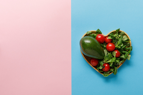 top view of fresh green vegetable salad in heart shaped bowl on pink and blue background - Photo, Image