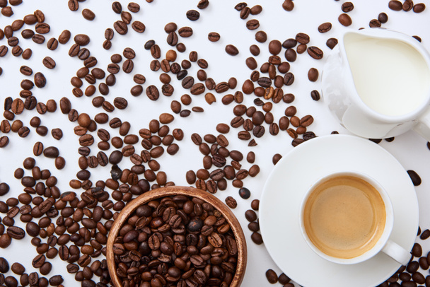 felülnézet a kávé csésze csészealj közelében szétszórt pörkölt bab, fa tál és a tej kancsó - Fotó, kép