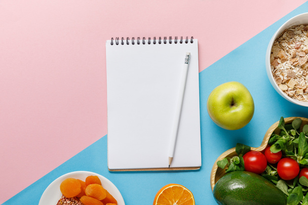 top view of empty notebook and pencil with delicious diet food on blue and pink background  - Photo, Image