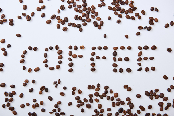 top view of coffee lettering made of brown coffee beans on white background - Фото, зображення