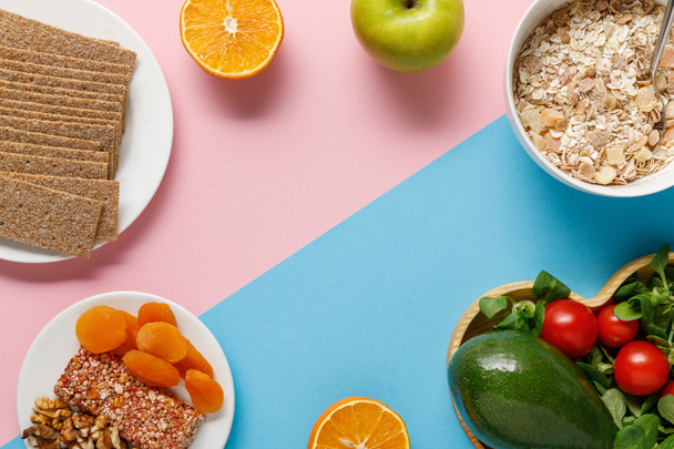 bovenaanzicht van heerlijke dieetvoeding en sportuitrusting op blauwe en roze achtergrond met kopieerruimte - Foto, afbeelding
