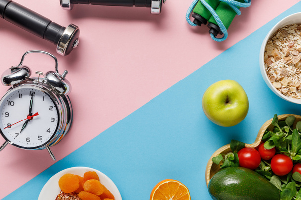 top view of delicious diet food and sport equipment with alarm clock on blue and pink background  - Photo, Image