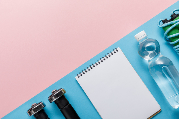 tendido plano con pesas, cuaderno vacío, botella de agua y saltar la cuerda sobre fondo rosa y azul
 - Foto, Imagen
