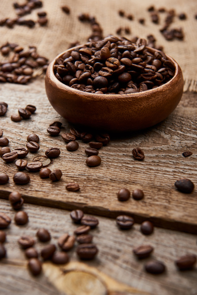 selective focus of fresh roasted coffee beans scattered near bowl on wooden board - Фото, изображение