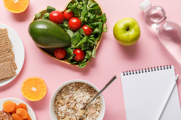 top view of fresh diet food, blank notebook with pencil and water on pink background - Photo, Image