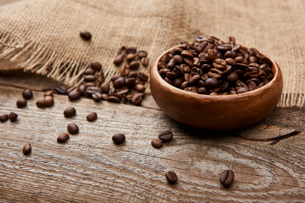 fresh roasted coffee beans in bowl near sackcloth on wooden board - Foto, Bild