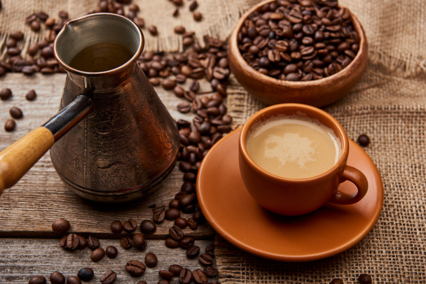 ziarna kawy w misce i dżezwa w pobliżu filiżanki kawy na drewnianym tle - Zdjęcie, obraz