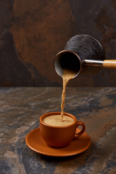 pouring coffee from cezve into brown cup on marble surface - Photo, Image