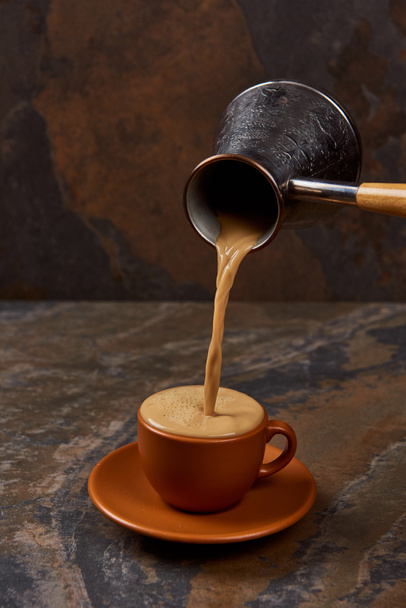 heißer leckerer Kaffee aus Cezve in Tasse auf Marmoroberfläche gießen - Foto, Bild