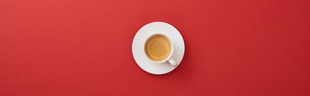 top view of white cup with fresh coffee on saucer on red background, panoramic shot - Fotó, kép