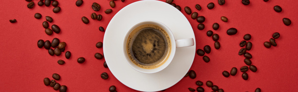panoramic shot of of delicious coffee in cup near scattered roasted beans on red background - Photo, Image