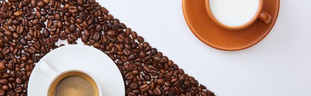 panoramic shot of delicious coffee in cup among roasted beans near cup of milk on white background - Фото, зображення