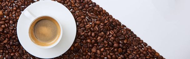 ロースト豆の近くのソーサーにカップでおいしいコーヒーのパノラマショット - 写真・画像