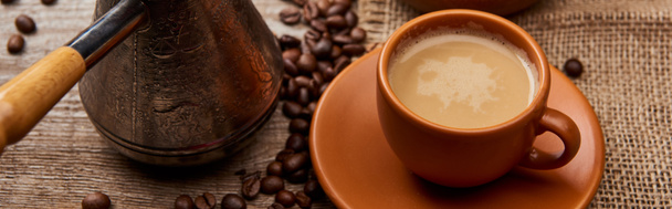 tiro panorâmico de grãos de café na tigela e cezve perto de xícara de café no fundo de madeira
 - Foto, Imagem