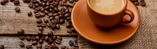 панорамний знімок кавових зерен біля чашки кави на дерев'яному фоні
 - Фото, зображення
