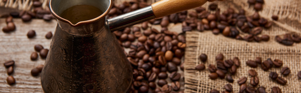 tiro panorâmico de cezve perto de grãos de café e saco em fundo de madeira
 - Foto, Imagem