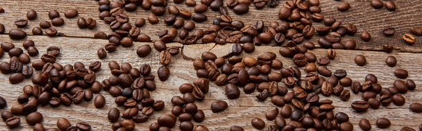 panoramic shot of wooden rustic table with scattered roasted coffee beans - Photo, Image