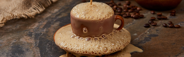 Panoramaaufnahme von frischem Kaffeeschaum, der aus Tasse auf Untertasse auf Marmoroberfläche strömt  - Foto, Bild