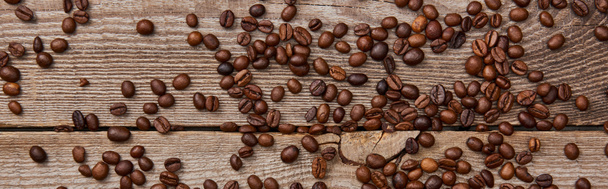 panoramic shot of wooden weathered table with scattered fresh roasted coffee beans - Photo, Image