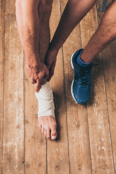 Schnappschuss eines Sportlers, der in einem Turnschuh sitzt und verletztes Bein in elastischem Verband berührt - Foto, Bild