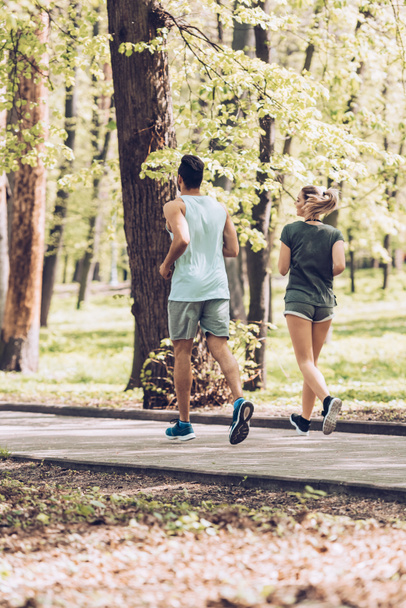 young sportsman and sportswoman running in green summer park - 写真・画像