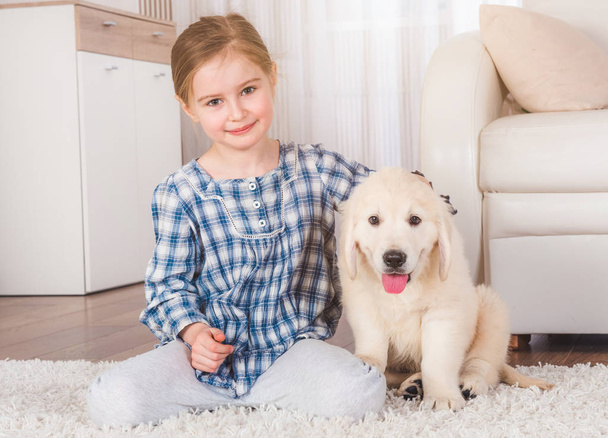 Smiling little girl sitting with retriever puppy - Фото, изображение
