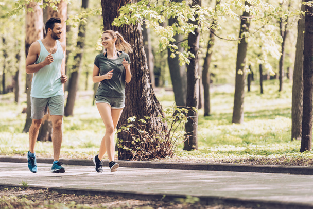 handsome man and attractive woman talking while running in park - Фото, зображення