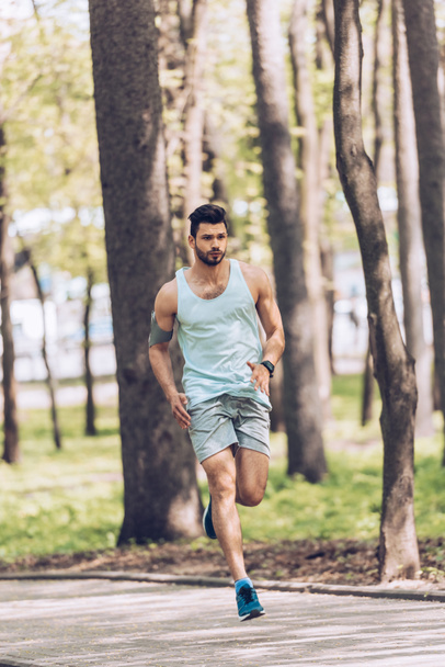 handsome man in sportswear running along pavement in park - Foto, Imagen