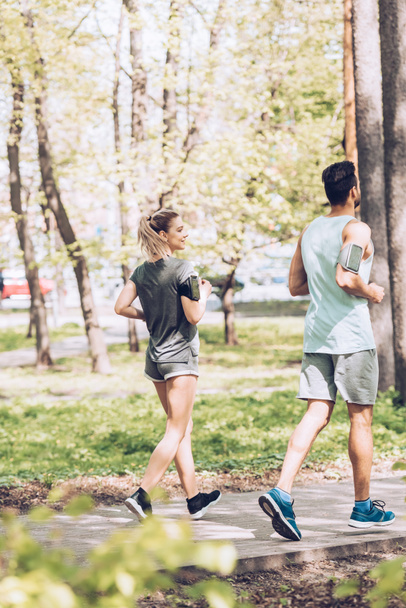 selective focus of young sportswoman and sportsman running together in park - Photo, Image