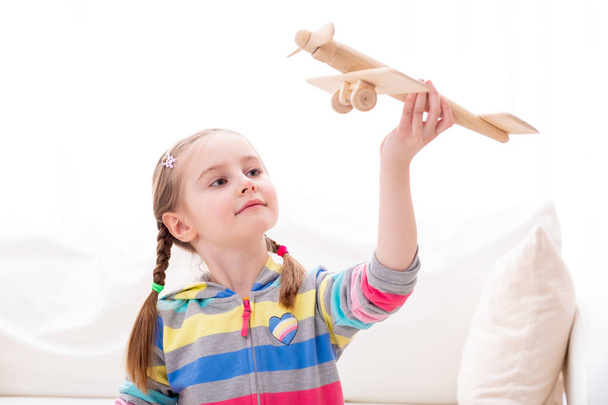 Gülen kız tahta oyuncak uçakla oynuyor. - Fotoğraf, Görsel