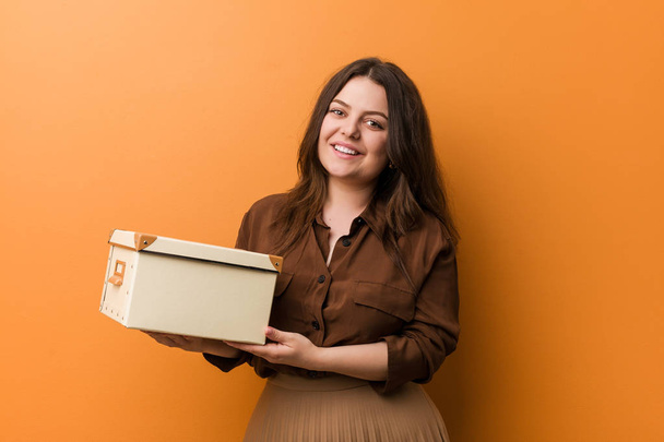Young curvy plus size woman holding a box happy, smiling and cheerful. - Photo, Image