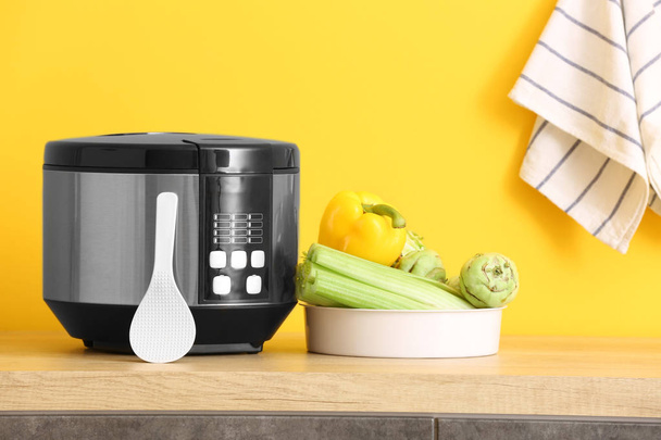 Modern multi cooker with vegetables on table against color background - Photo, image