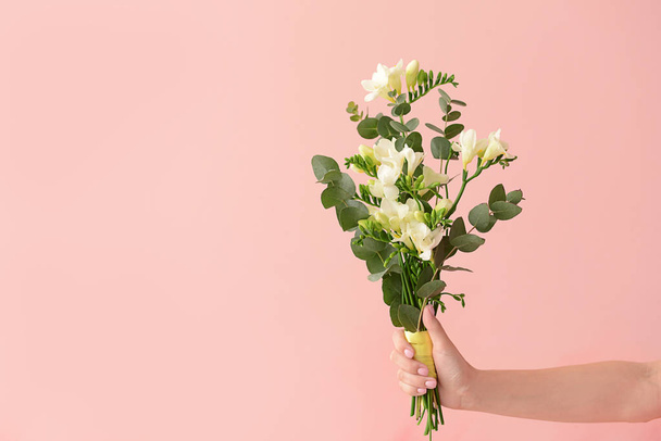 Θηλυκό χέρι με όμορφη φρέζια λουλούδια στο φόντο χρώμα - Φωτογραφία, εικόνα