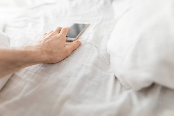 Male hand reaches to smartphone immediately after wake up in bed - Fotó, kép