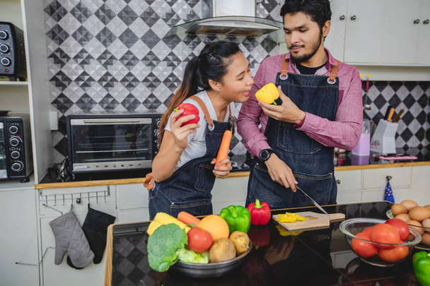 glückliches und lächelndes junges Paar beim Kochen in der heimischen Küche - Foto, Bild