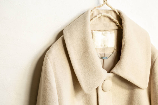 abrigo de lana beige colgando de la percha de ropa sobre fondo blanco
 - Foto, imagen