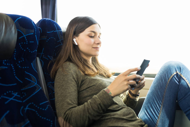 Молодая женщина слушает музыку на смартфоне во время путешествия в автобусе
 - Фото, изображение